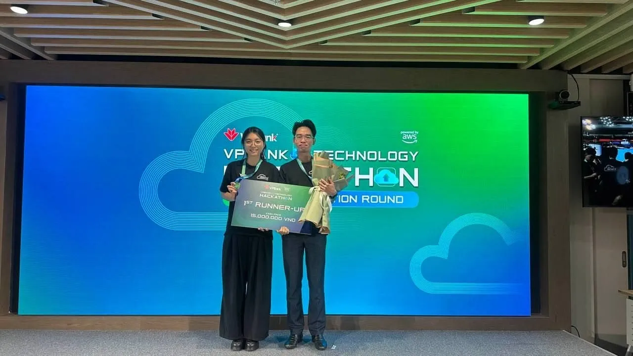 Hai người cầm tấm bảng 1ST RUNNER-UP trước màn hình VPBank Technology Hackathon trong một phòng họp